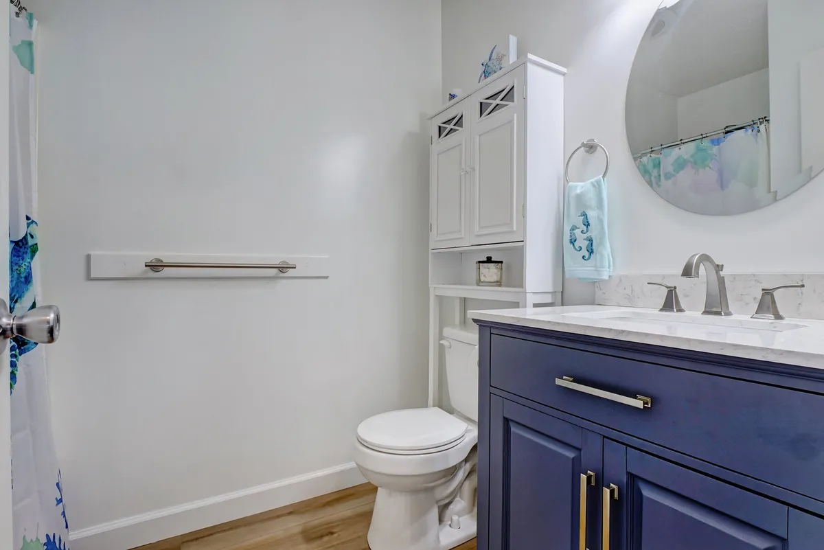 A refreshing and clean bathroom with dark blue cabinetry, a framed mirror, and a storage cabinet. The space feels inviting and functional, making it suitable for morning routines and guest use.