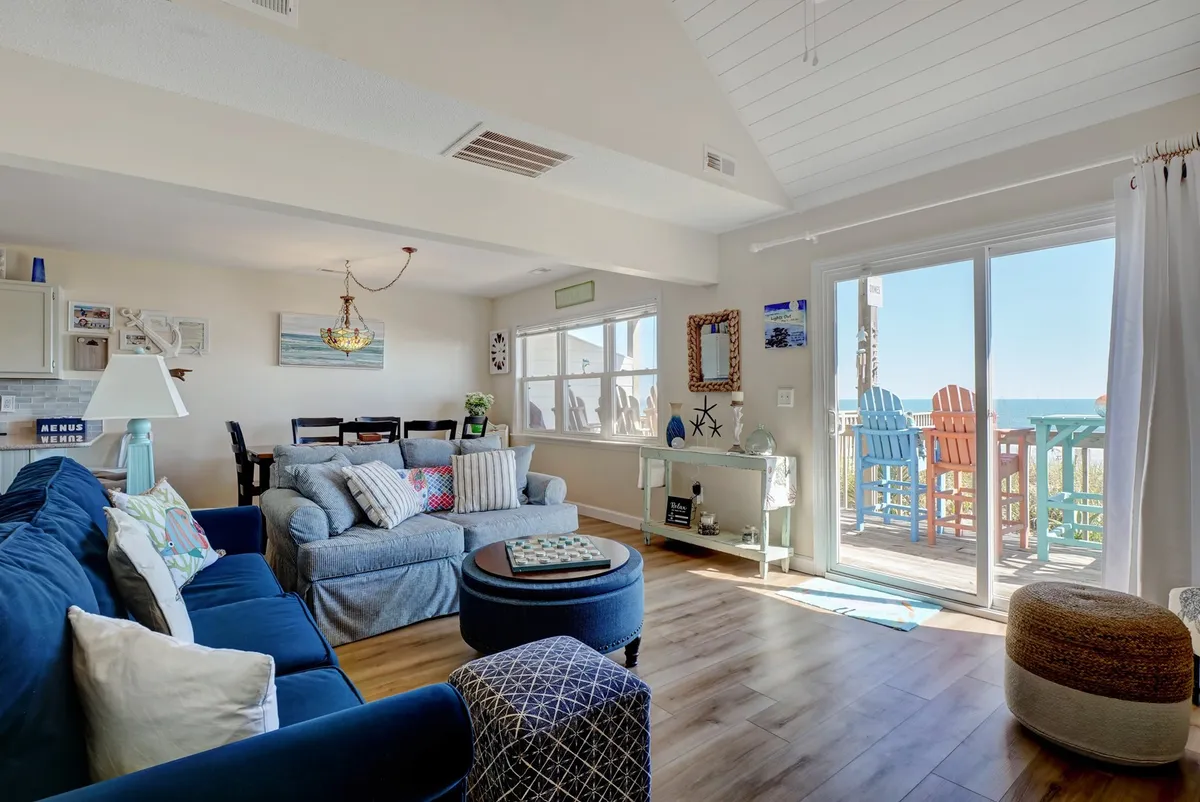 A bright, open living and dining area featuring a comfortable blue sofa, a family-sized dining table, and a sliding glass door that opens onto the deck. The space is ideal for relaxing, socializing, and making lasting memories with loved ones.