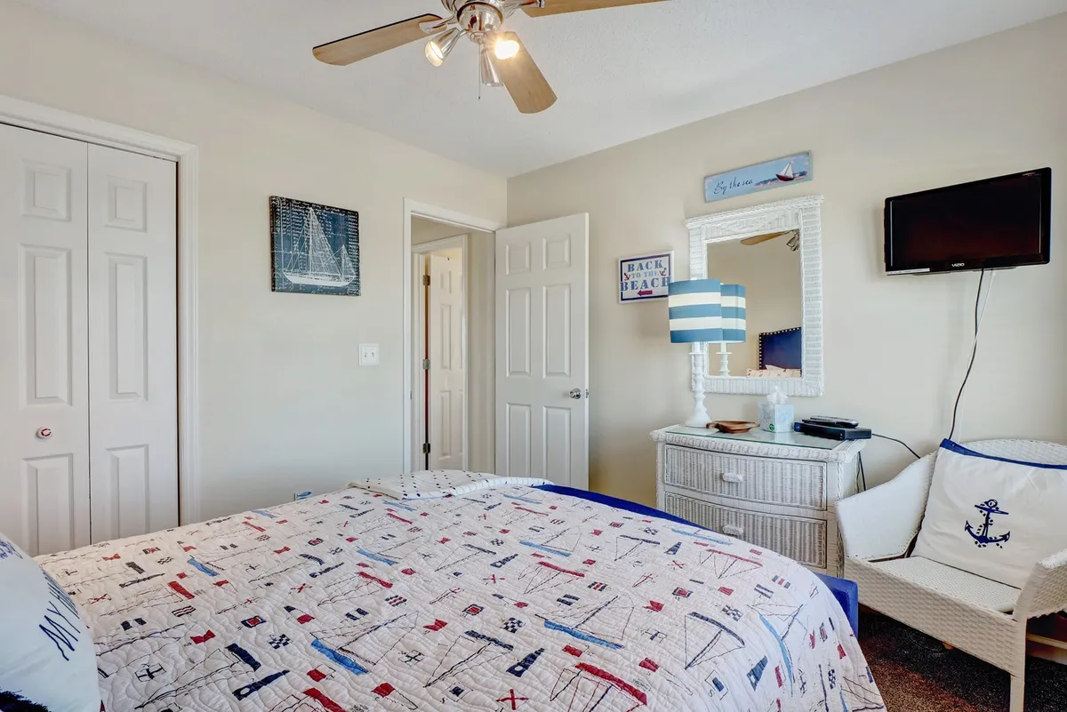 A tranquil bedroom with a nautical-themed quilt, blue-striped lamp, and a cozy chair by the window. The room is thoughtfully decorated and offers a serene space to relax, read, or enjoy a quiet morning coffee.