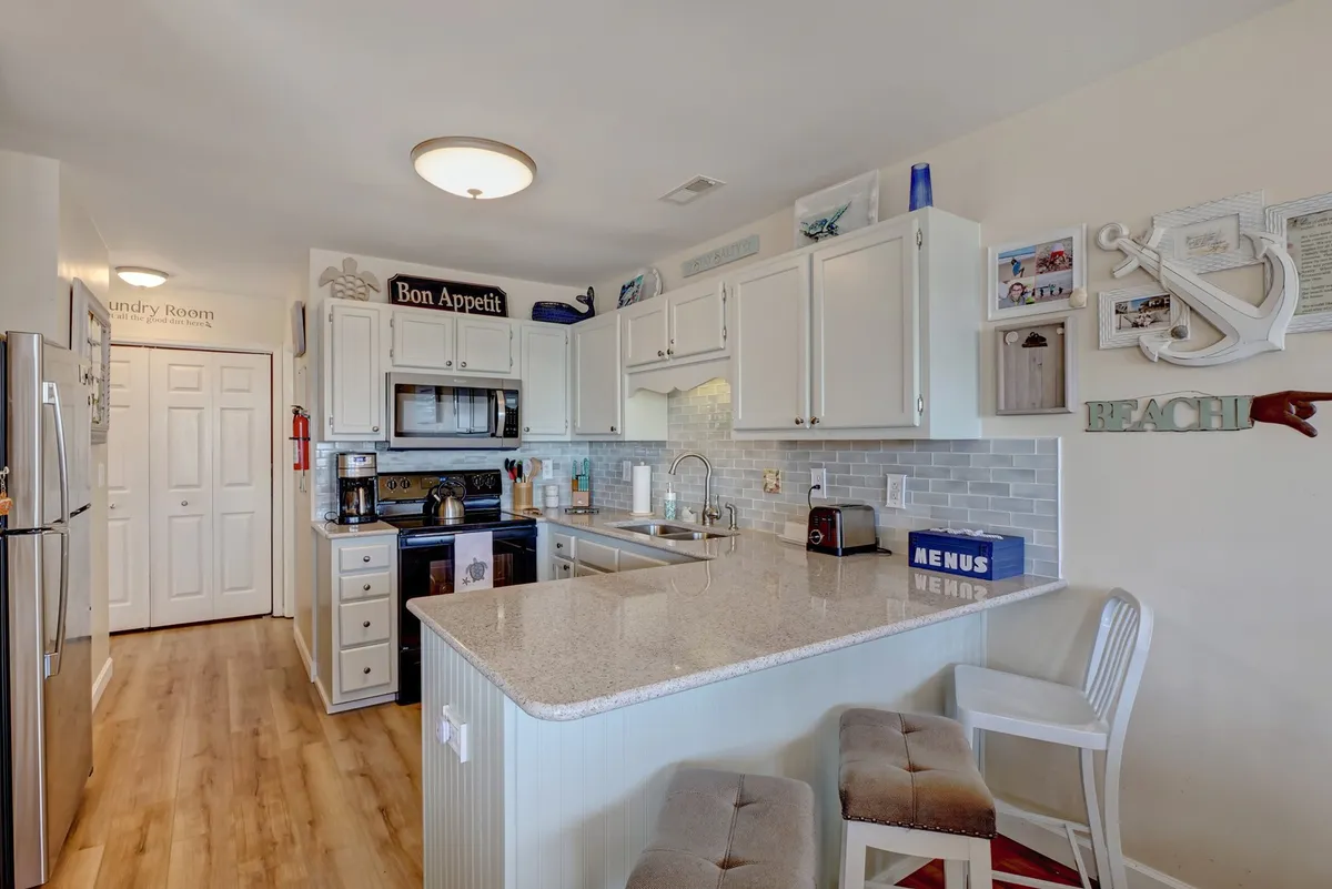A modern kitchen with a prominent kitchen island, white cabinetry, stainless steel appliances, and decorative wall art. The space is bright and designed for both cooking and socializing, inviting guests to gather and interact.