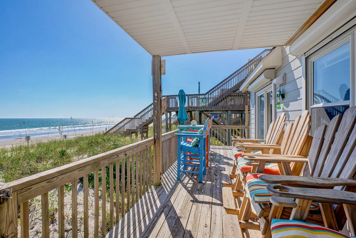 A spacious wooden deck furnished with colorful Adirondack chairs, all positioned to face an expansive ocean view. The bright chairs invite relaxation, while the deck’s open railings offer unobstructed vistas of the waves and coastal horizon. Soft sunlight bathes the space, suggesting both morning tranquility and sunset gatherings.