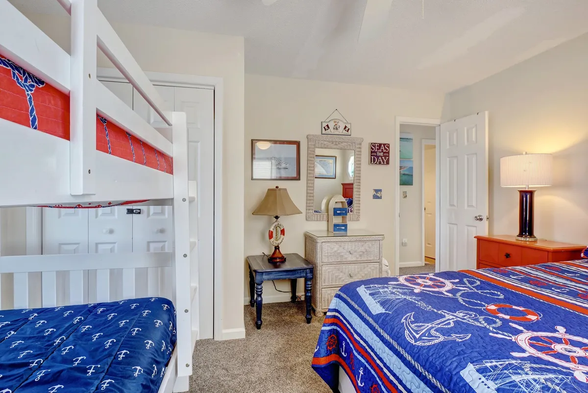 A playful, family-oriented bedroom featuring a double bed and bunk beds adorned with nautical-themed bedding. The room includes a decorative lamp and a mirror, while the playful mood is enhanced by the suggestion of family bonding and children's activities.